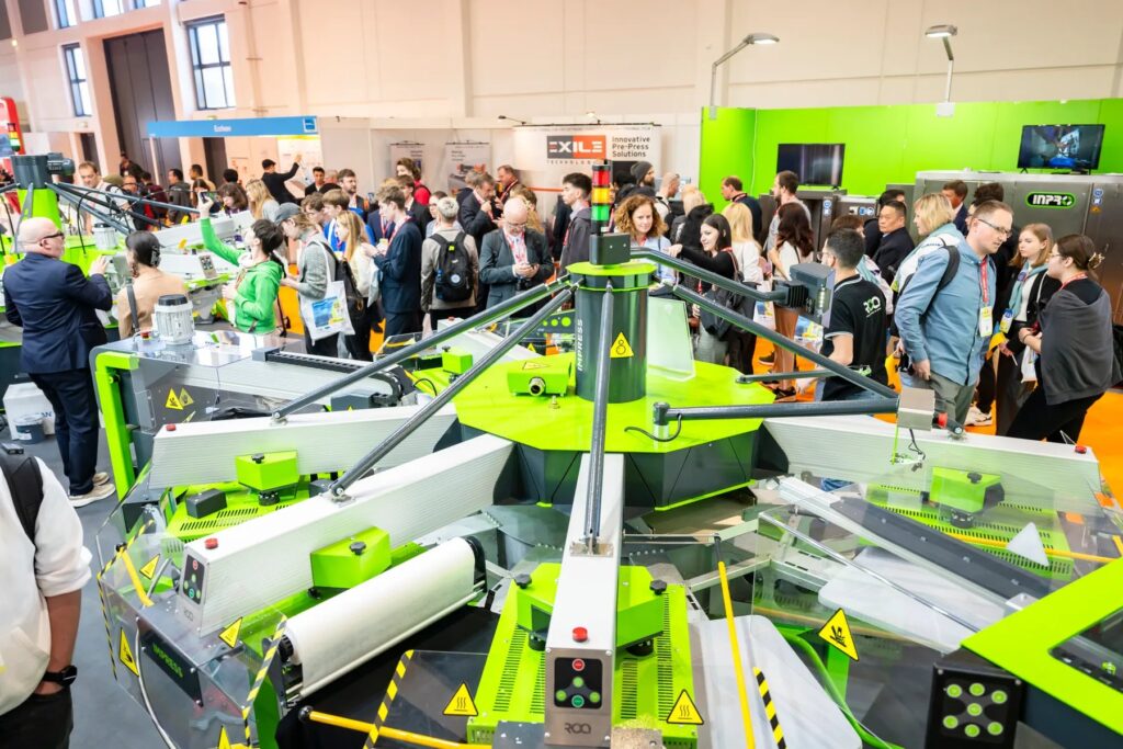 Visitors gather around a carousel screen printing press on the textile show floor at FESPA Global Print Expo