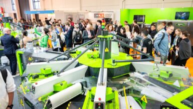 Visitors gather around a carousel screen printing press on the textile show floor at FESPA Global Print Expo